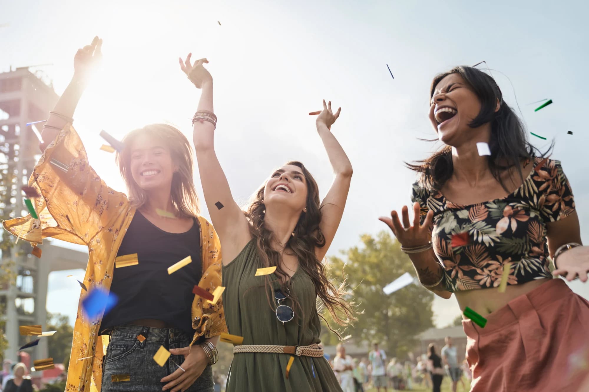 Drei Menschen feiern bei einem sommerlichen Outdoor-Event unter fliegendem Konfetti